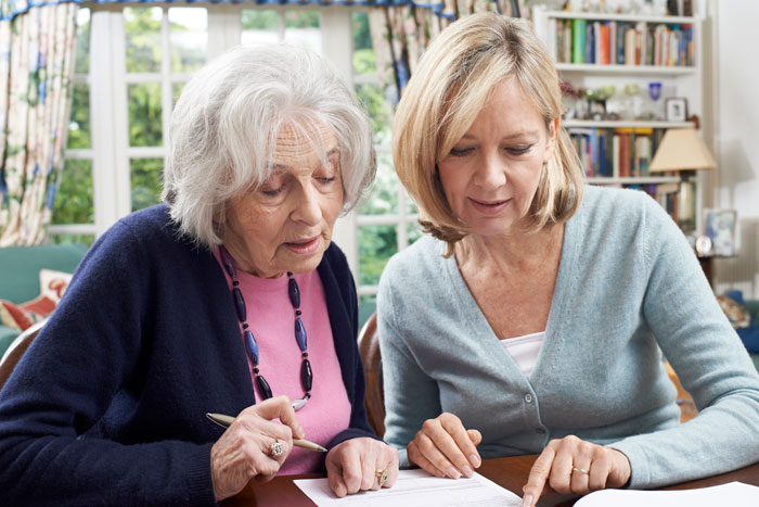 elderly woman receiving help signing up for medigap coverage with forms from her daughter