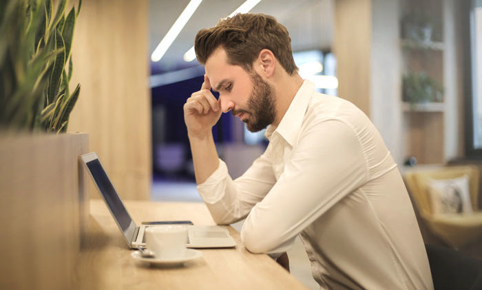 Young male professional dealing with work stress while working on laptop in office